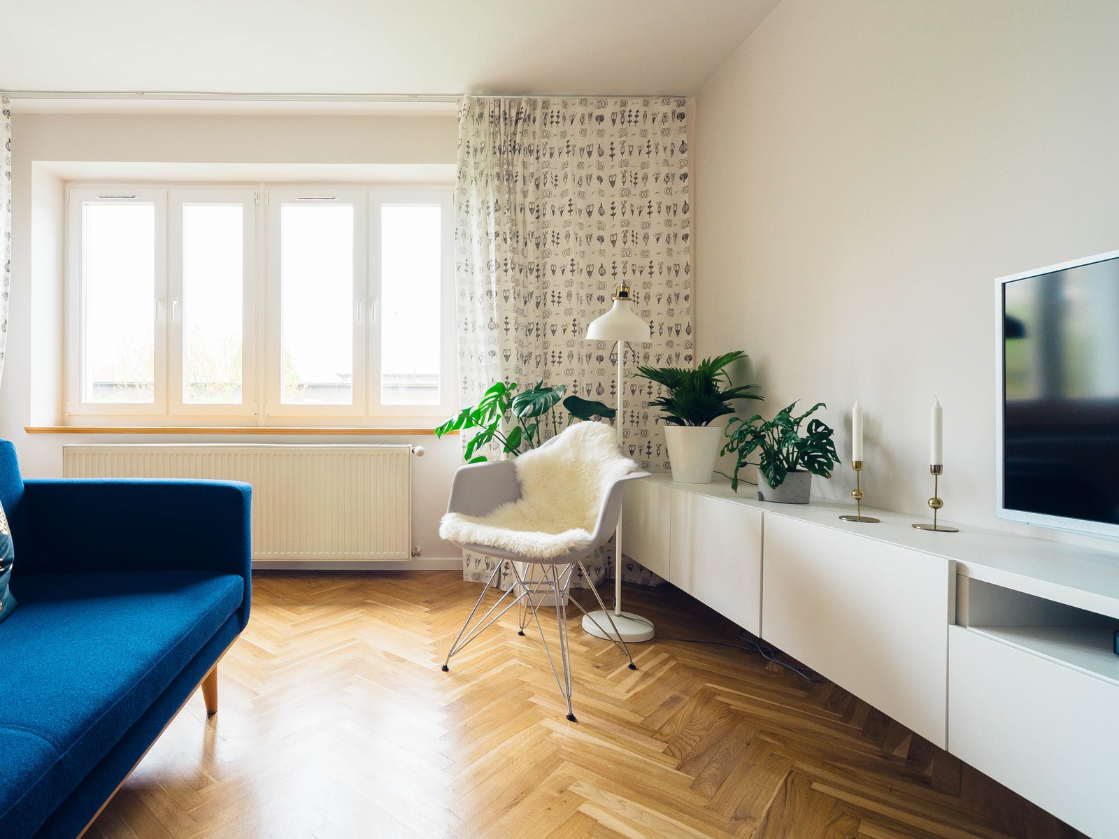 A bright, considered living room with herringbone wood flooring, layered lighting, curtains and a styled console — the standard of finish this drawing set is built toward.